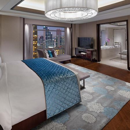 מלון Mandarin Oriental, קואלה לומפור מראה חיצוני תמונה The photo shows a luxurious hotel room featuring a spacious layout with modern decor. In the foreground, there is a large bed with a light-colored headboard and a blue decorative throw blanket. The bed is positioned on a stylish wooden floor adorned 