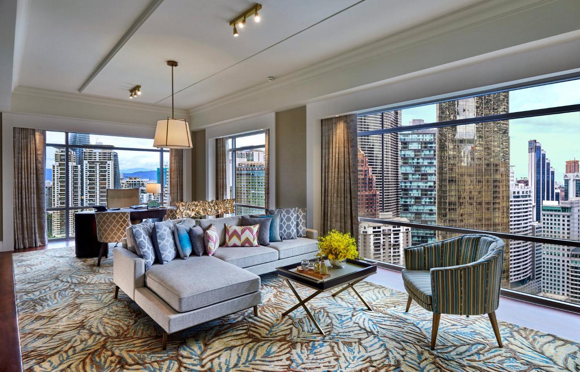 מלון Mandarin Oriental, קואלה לומפור מראה חיצוני תמונה The photo showcases a modern and stylish living room with large windows that offer a view of city skyscrapers. The room features a light gray sectional sofa adorned with colorful cushions, a coffee table with a floral arrangement, and a comfortable a