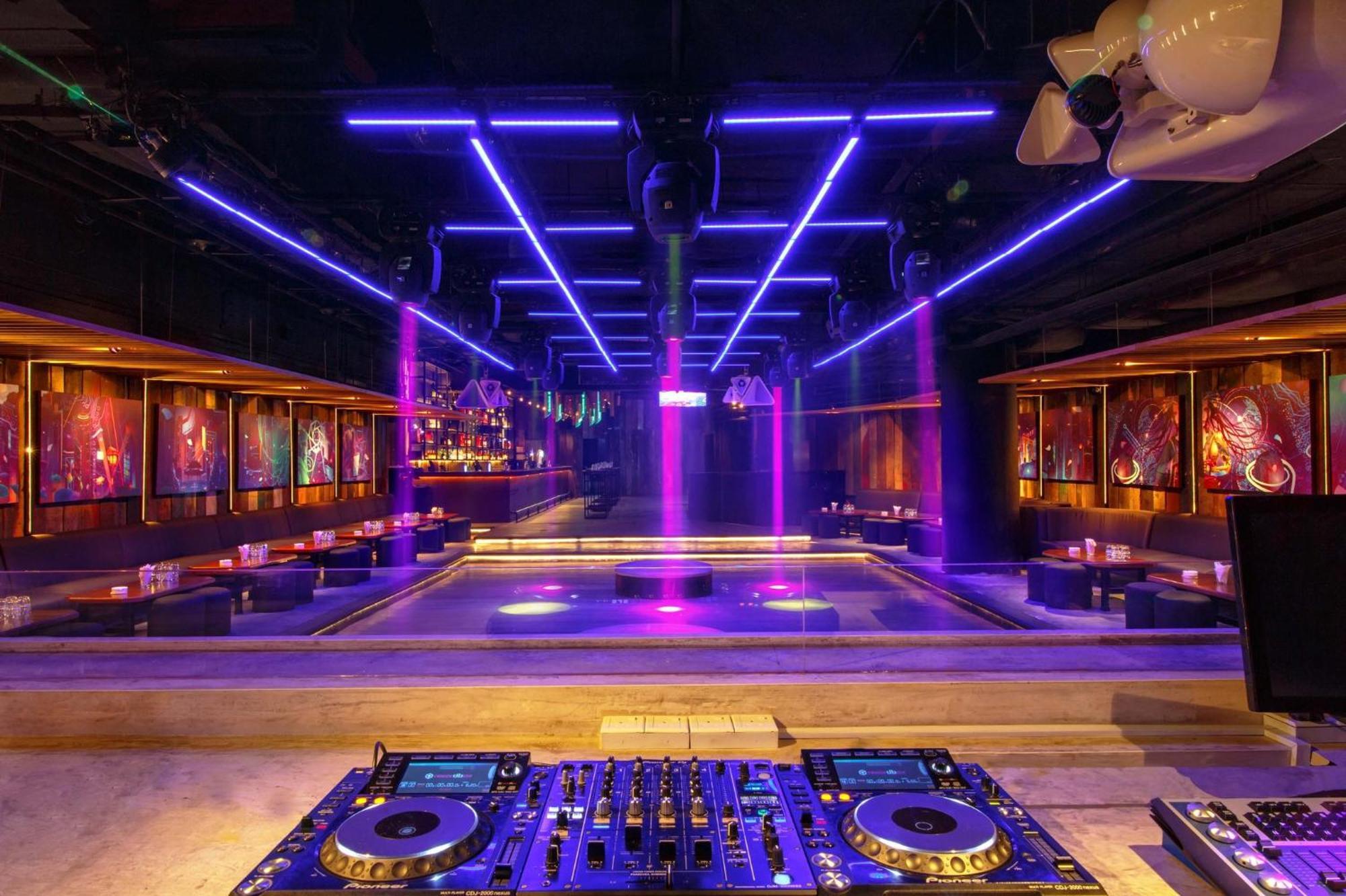 מלון Mandarin Oriental, קואלה לומפור מראה חיצוני תמונה The photo depicts a modern nightclub interior. In the foreground, there is a DJ setup with turntables and mixers. The main area features a spacious dance floor illuminated by vibrant purple lights and neon lines overhead. Surrounding the dance floor 