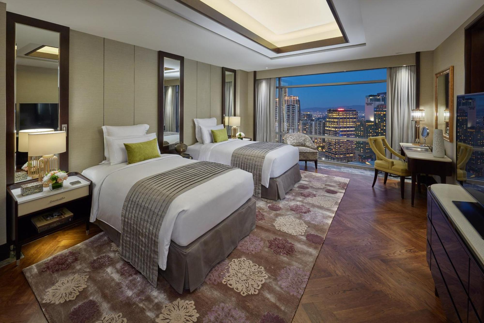 מלון Mandarin Oriental, קואלה לומפור מראה חיצוני תמונה The photo shows a luxurious hotel room featuring two beds with white linens and decorative throws. The room has a modern and elegant design, with soft lighting and large windows that provide a view of a city skyline, likely at dusk. There are mirrors