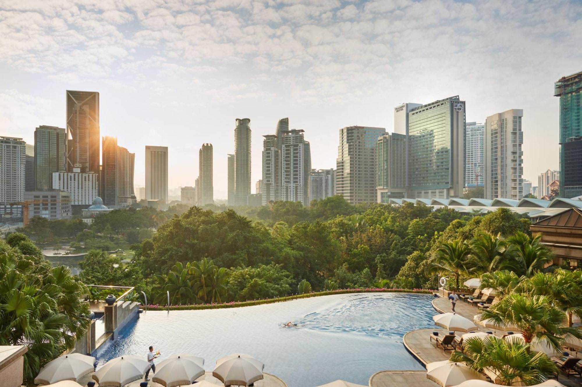מלון Mandarin Oriental, קואלה לומפור מראה חיצוני תמונה The photo shows a panoramic view of a modern city skyline during sunrise. In the foreground, there's an infinity pool with a clear blue water, bordered by lounge chairs and umbrellas. The background features a variety of tall buildings, showcasing a 
