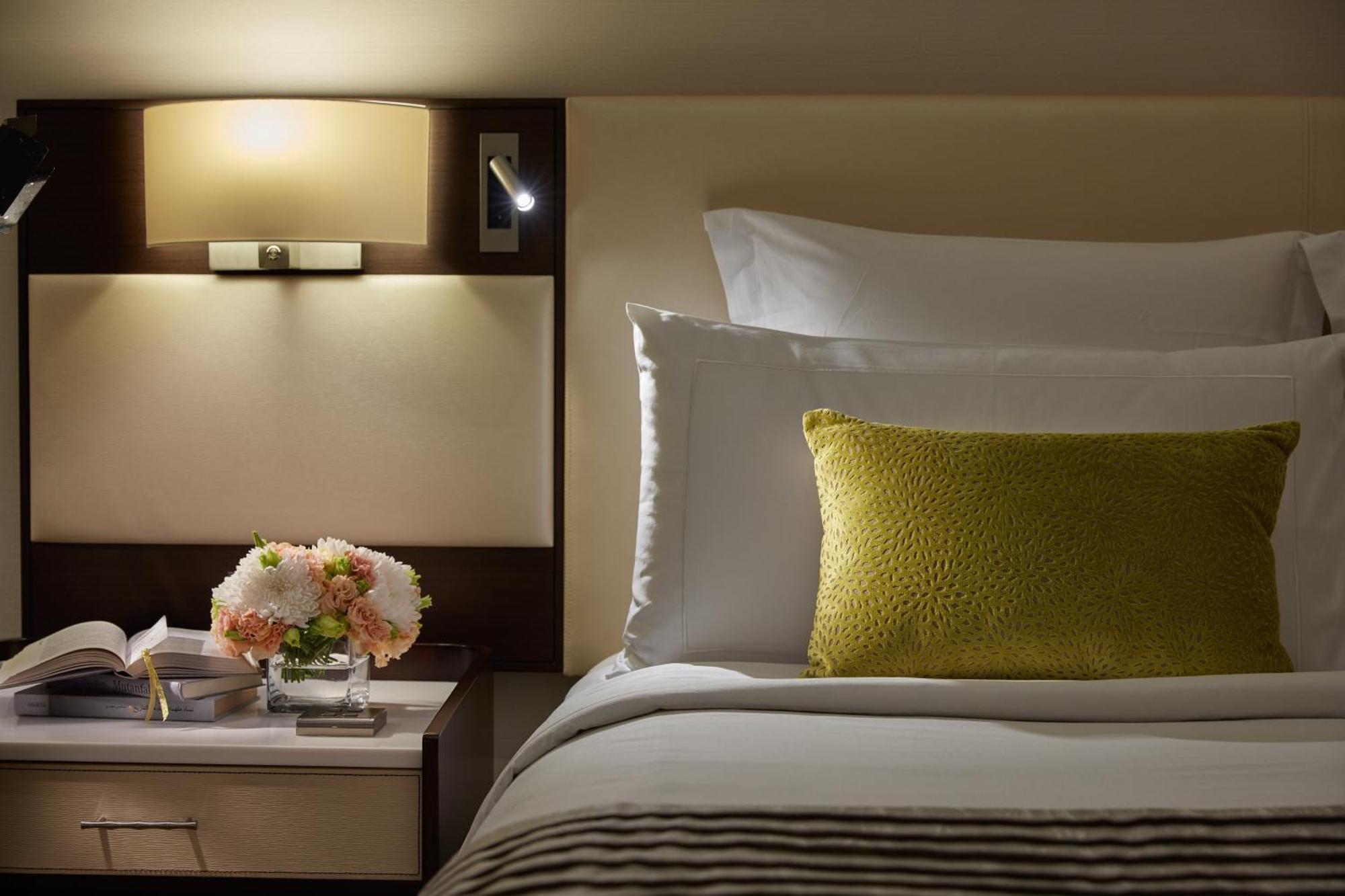 מלון Mandarin Oriental, קואלה לומפור מראה חיצוני תמונה The photo depicts a cozy and elegant bedroom setting. The bed is made with crisp white linens and features a decorative yellow-green pillow. Next to the bed, there is a small nightstand with a vase of fresh flowers, likely in soft pastel colors. A bo