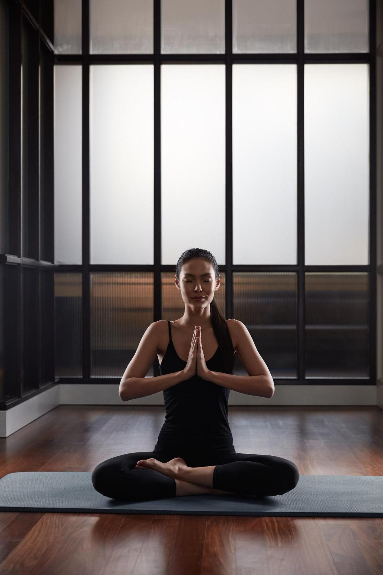 מלון Mandarin Oriental, קואלה לומפור מראה חיצוני תמונה The photo shows a woman practicing yoga or meditation. She is in a serene environment, possibly indoors, with large windows that allow soft light to filter in. The woman is seated with her hands pressed together in a prayer position at her chest, and