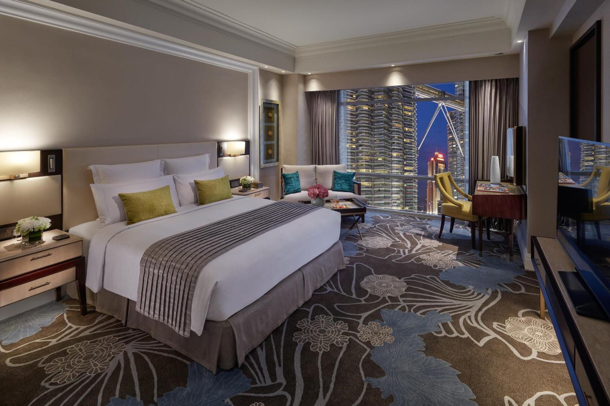 מלון Mandarin Oriental, קואלה לומפור מראה חיצוני תמונה The photo shows a luxurious hotel room featuring a large bed with decorative pillows and a plush headboard. The room is decorated in neutral tones with floral patterns on the carpet. To the side of the bed, there are two stylish chairs and a small ta