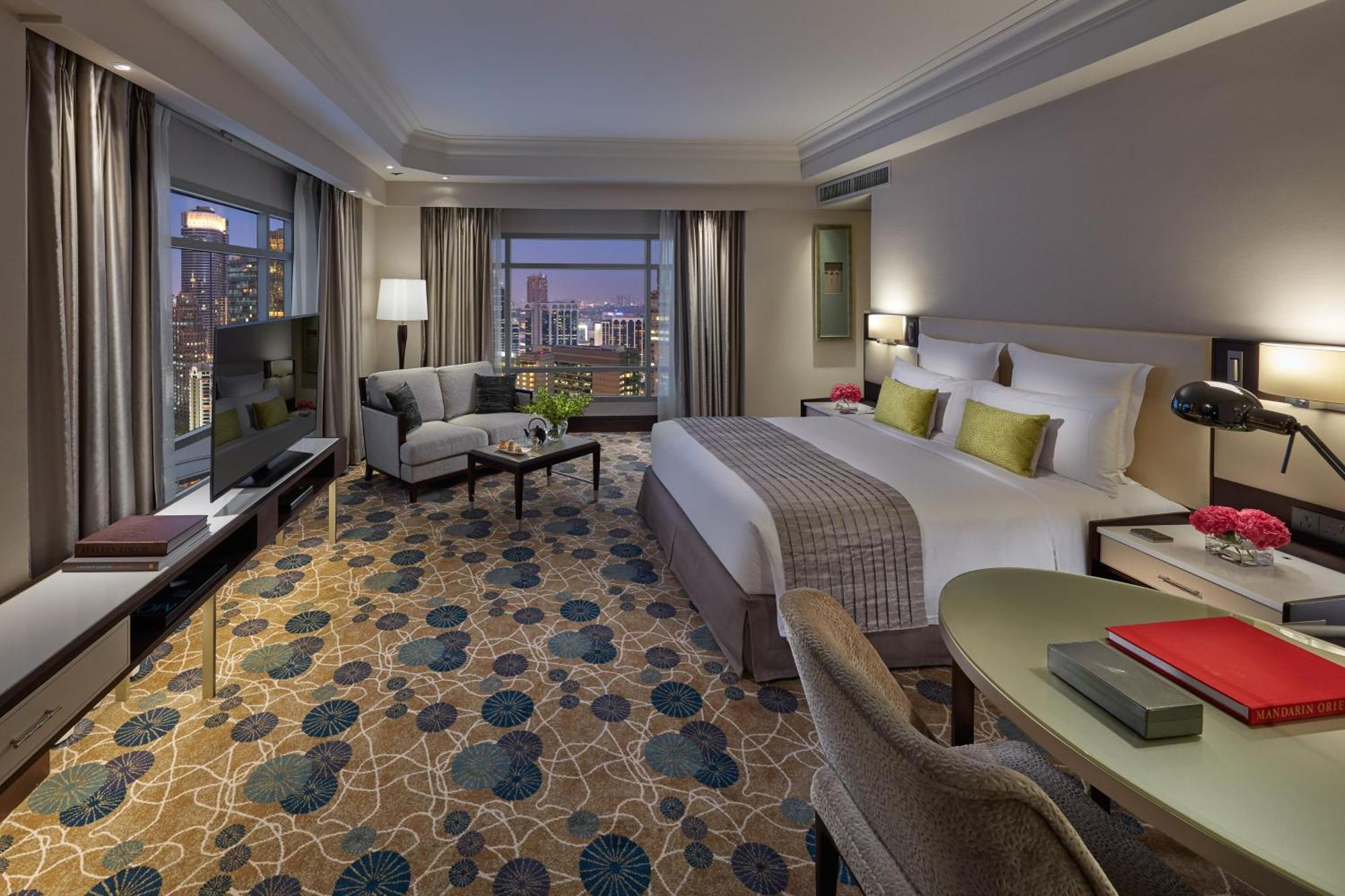 מלון Mandarin Oriental, קואלה לומפור מראה חיצוני תמונה The photo shows a modern hotel room that features a king-sized bed with light-colored bedding and decorative pillows. There is a comfortable seating area with a gray armchair and a small table, along with a desk and a chair. A flat-screen television 