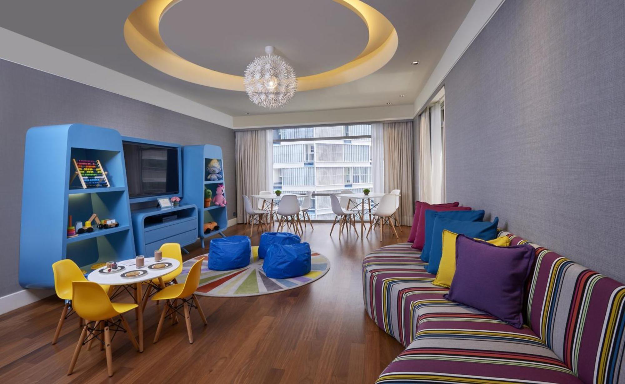מלון Mandarin Oriental, קואלה לומפור מראה חיצוני תמונה The photo shows a modern, colorful living space designed for a playful atmosphere. It features a curved couch with striped upholstery in various colors, complemented by vibrant throw pillows. There's a round coffee table with a set of small chairs in