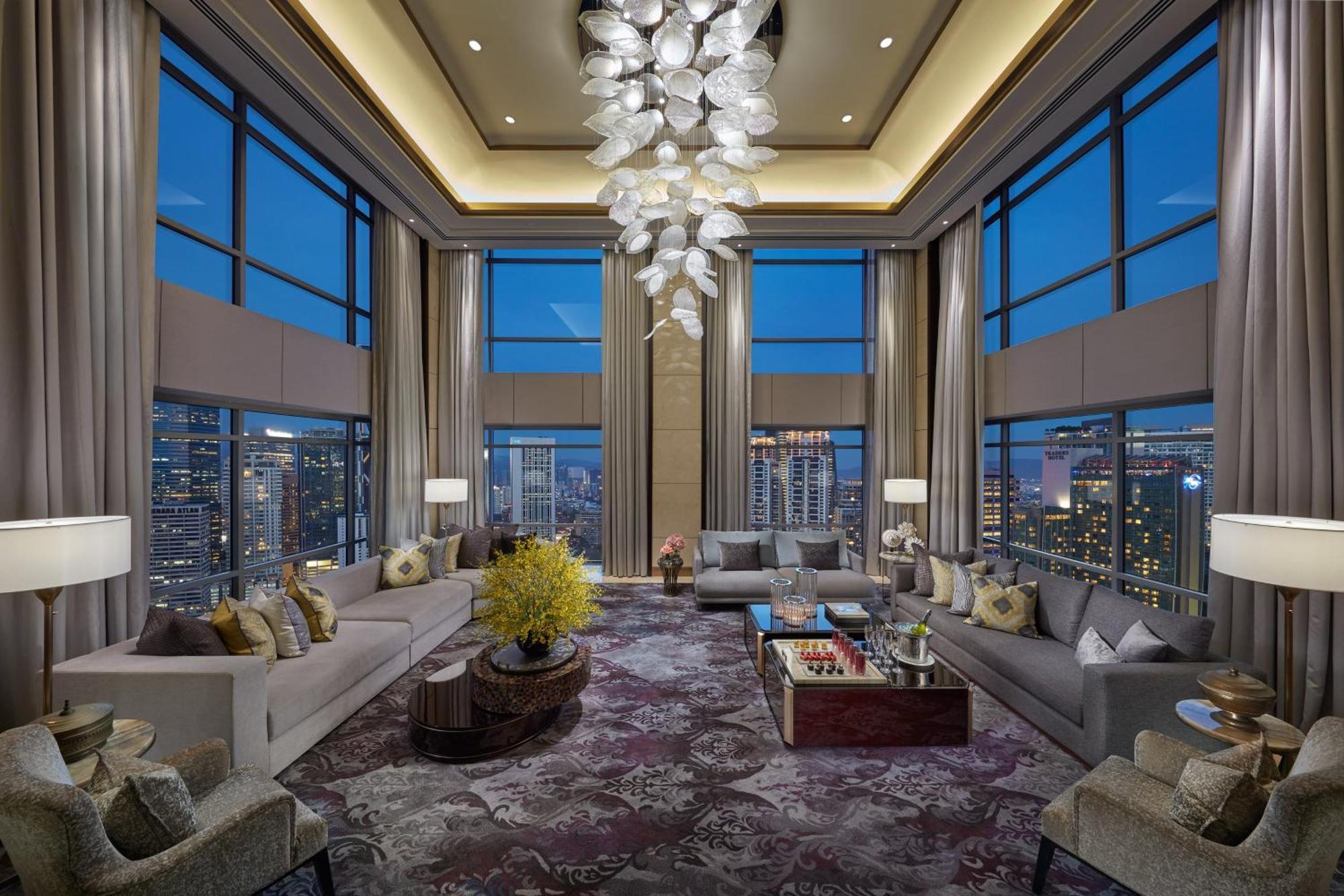 מלון Mandarin Oriental, קואלה לומפור מראה חיצוני תמונה The photo showcases a luxurious living room featuring large floor-to-ceiling windows that provide a stunning view of the city skyline at dusk. The room is elegantly furnished with modern sofas, accent chairs, and a stylish coffee table. A prominent c