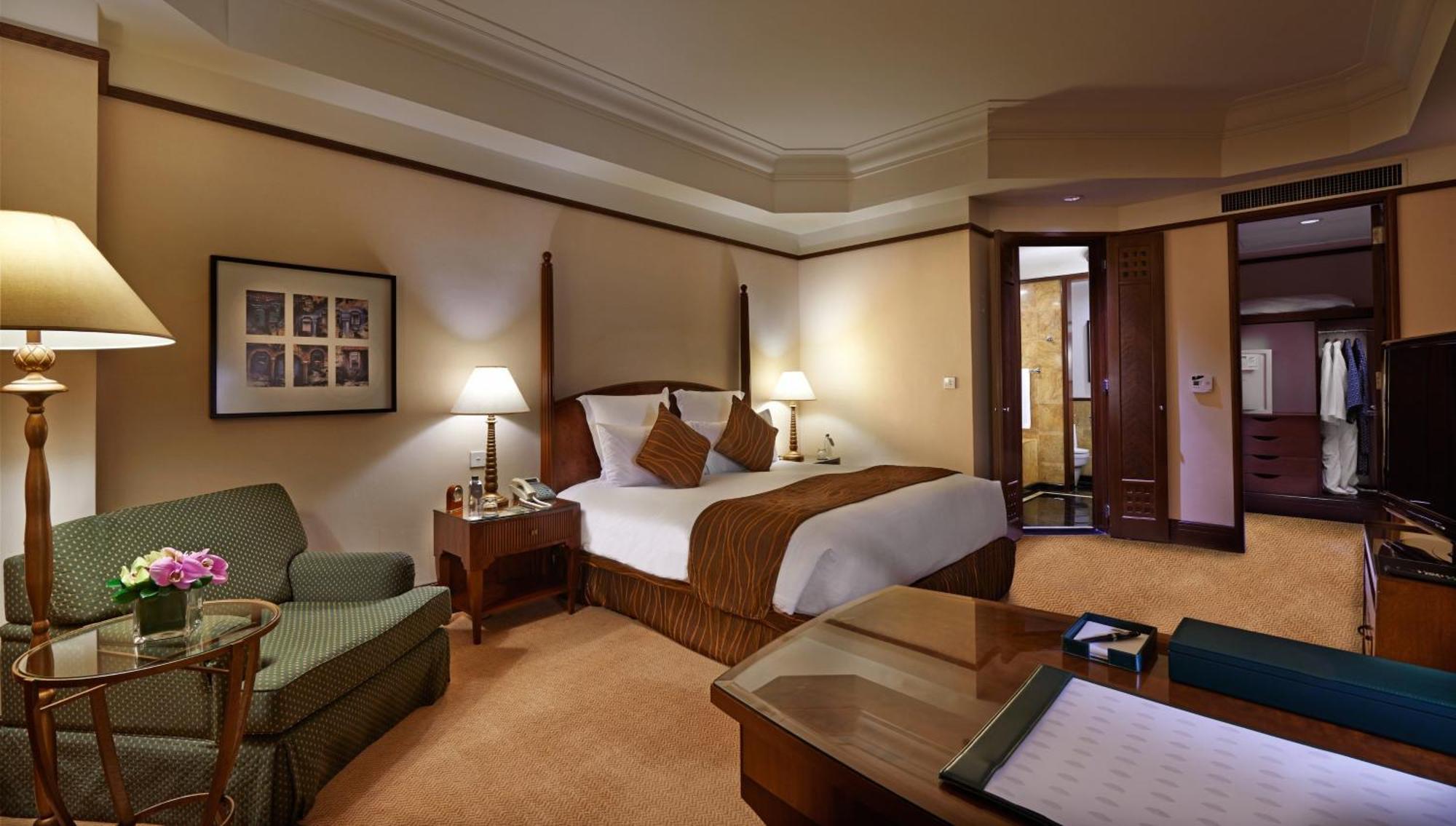 מלון Mandarin Oriental, קואלה לומפור מראה חיצוני תמונה The photo depicts a luxurious hotel room. It features a large bed with decorative pillows, flanked by two bedside tables with lamps. To the side, there is a green upholstered armchair and a coffee table. The room has warm-colored walls and a plush ca