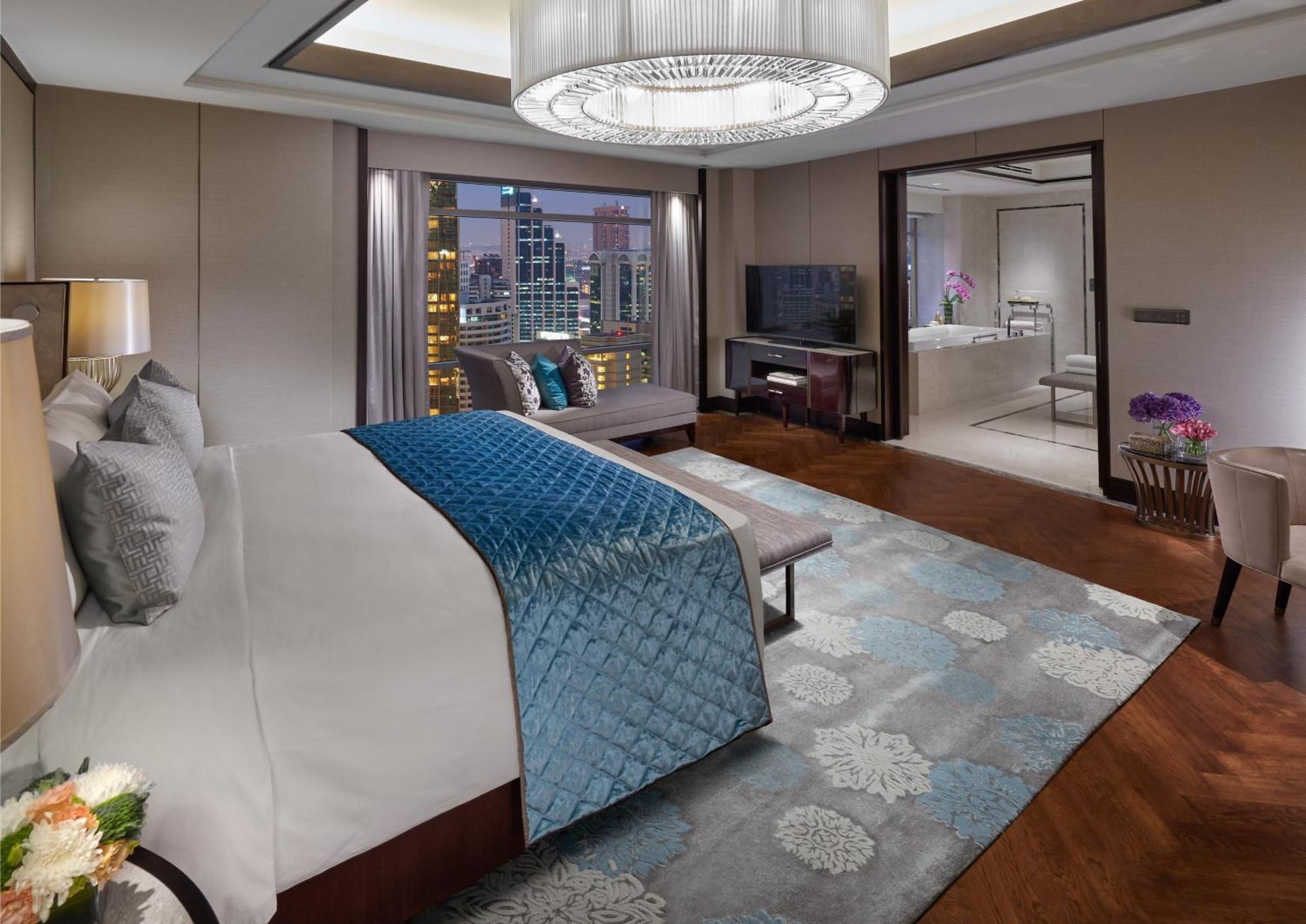 מלון Mandarin Oriental, קואלה לומפור מראה חיצוני תמונה The photo shows a luxurious hotel room featuring a spacious layout with modern decor. In the foreground, there is a large bed with a light-colored headboard and a blue decorative throw blanket. The bed is positioned on a stylish wooden floor adorned 