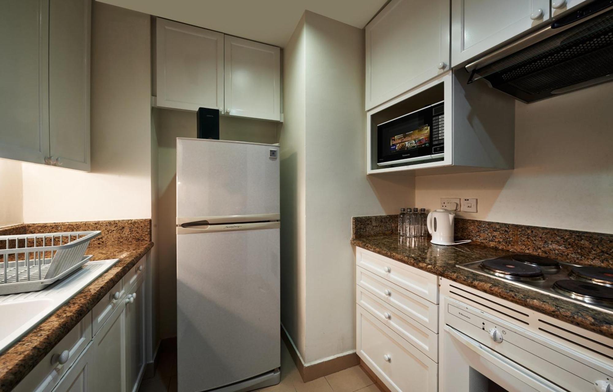 מלון Mandarin Oriental, קואלה לומפור מראה חיצוני תמונה The photo shows a compact kitchen featuring modern appliances. There is a refrigerator on the left side, a microwave mounted above a countertop, and a stove integrated into the countertop. The cabinets above and below are finished in light colors, pr